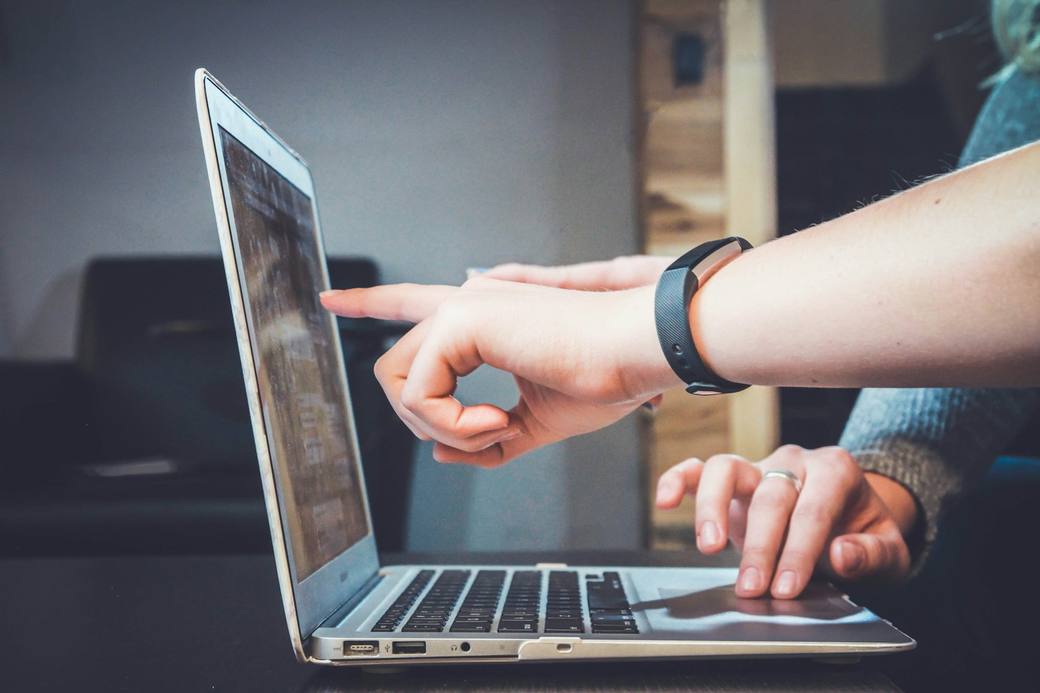 Hands typing on a laptop keyboard with code on the screen